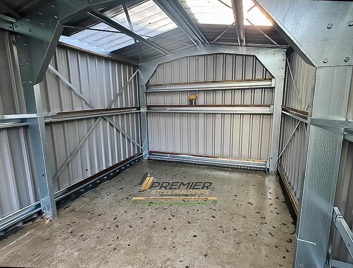 The empty interior of a small steel shed showing the galvanized frame, wall girts, and internal cross-bracing.