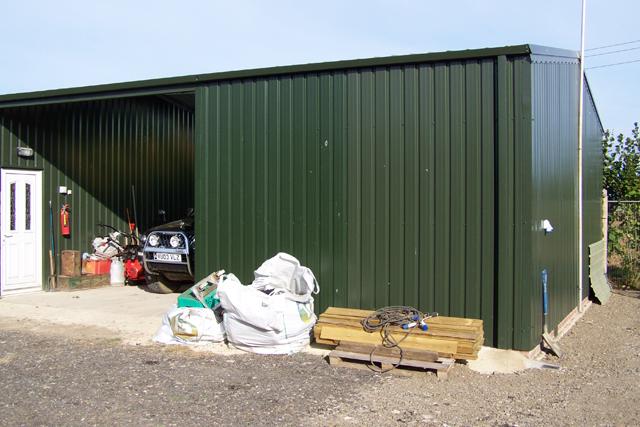 A dark green building with random items stored outside