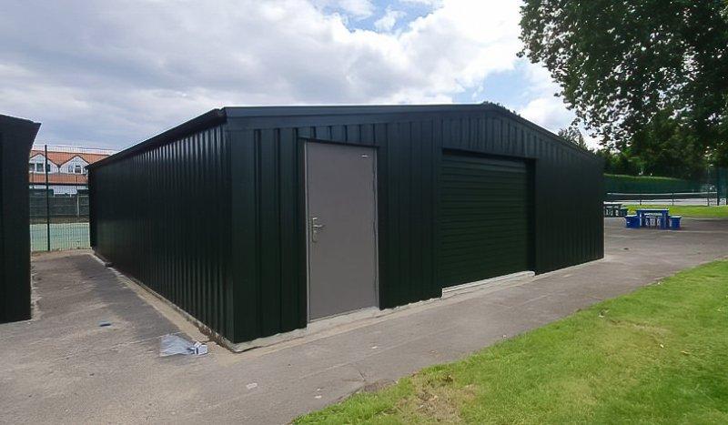 Angle view of a green corrugated metal shed with a grey side door and closed front roller door.