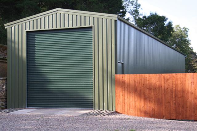 A narrow green building next to a wooden fence
